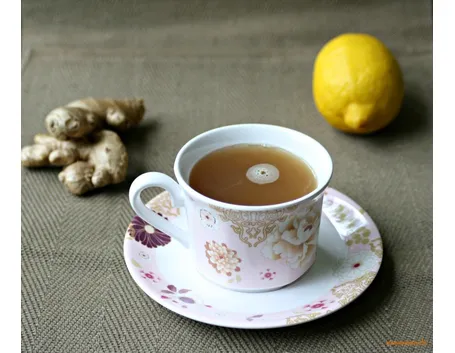 Tazza di decotto di zenzero con accanto pezzi di radici e un limone