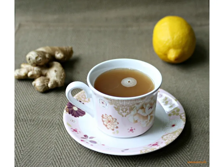 Tazza di decotto di zenzero con accanto pezzi di radici e un limone