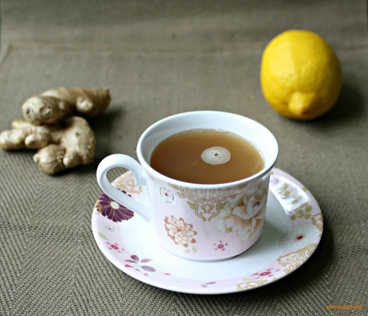 Tazza di decotto di zenzero con accanto pezzi di radici e un limone